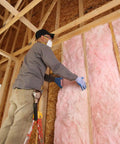 Worker installing Sweet Deal 10 Bag Bundle of R-15 Kraft Faced Fiberglass Insulation with Vapor Barrier in wall.