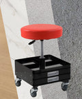 Rolling stool with red round padded seat on chrome post atop black tool cart with two drawers and four casters.