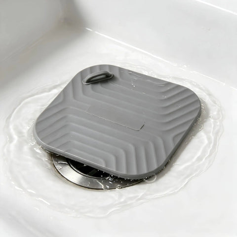 Shower Drain Cover Tub Stopper Square Silicone Floor Drain Cover resting on a shower drain, showing flexible gray silicone material.