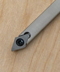 Close-up of carbide woodturning tool head with square gray cutter and screw on wood surface