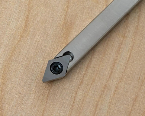 Close-up of carbide woodturning tool head with square gray cutter and screw on wood surface