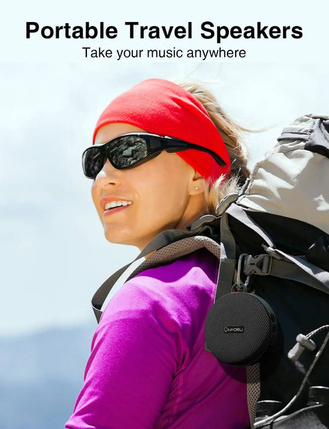 Woman hiking with portable travel speaker attached to backpack, showcasing compact design for outdoor use.