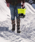 Person using All Season Handheld Seed And Fertilizer Spreader For Lawns, 18V Battery Compatible, spreading salt on snowy path