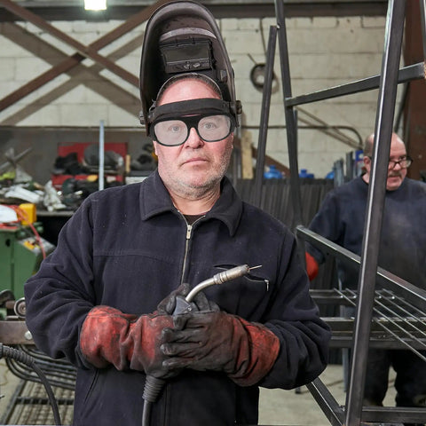 Built Dog Gone Tough 6-Pack Welding Goggles Featuring Auto Darkening Lenses For Serious Shop Work snug fit on a worker in gloves holding welding tools.