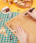 Person tracing with a pen on a wooden board using Slick Clear Acrylic Mountain Router Template For Precision Wood Inlay Projects Features Built Different Anti Scratch Layer To Level Up Your Charcuterie Board Sign Crafting Game.