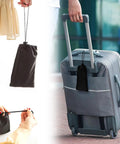 Person holding a drawstring bag containing the 2 Pack Foot Hammock For Plane Travel Portable Airplane Foot Rest Leg Hammock For Long Flights Adjustable Plane Footrest Foot Sling For A Comfy Flying Experience And Back Relief On Extended Air Travel, hanging from a suitcase