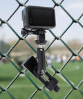 Fence Mount For Cell Phones And Action Cameras On Chain Link Fence Attaches To Baseball Softball Tennis Fences For iPhone GoPro Insta360 Mevo Start Recording Clip Holder With Strong Knob Fixation For Stable Secure Shots During Rugged Play shown attached to a chain link fence with a field in the background.