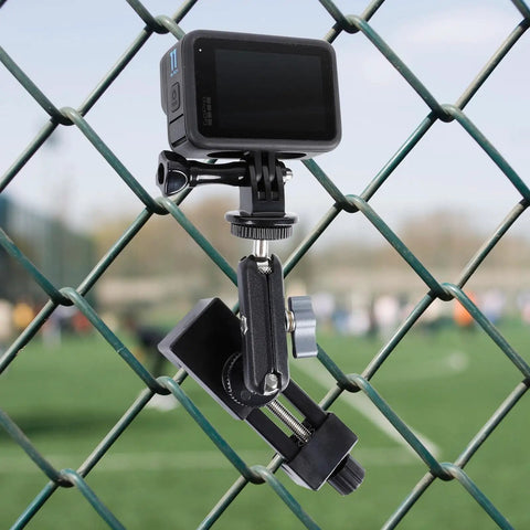 Fence Mount For Cell Phones And Action Cameras On Chain Link Fence Attaches To Baseball Softball Tennis Fences For iPhone GoPro Insta360 Mevo Start Recording Clip Holder With Strong Knob Fixation For Stable Secure Shots During Rugged Play shown attached to a chain link fence with a field in the background.