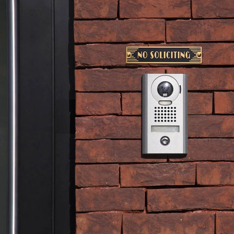 Brick wall with mounted brass No Soliciting sign six point five inch classic art deco style with brushed matte finish.
