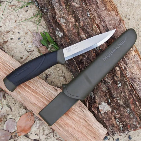 Companion Carbon Steel Fixed Blade Knife With Sheath 4.1 Inch Blade Military Green resting on log outdoors.