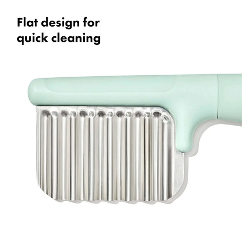 OXO Tot crinkle cutter for kids with mint-green handle and stainless steel ribbed blade, close-up view.