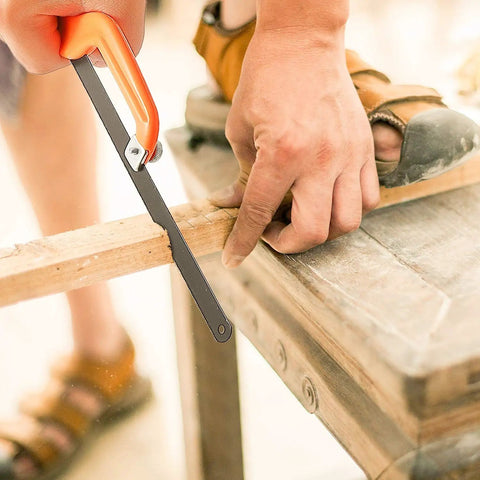 Close-up of hacksaw set with 12 inch steel frame replaceable blades and metal miter guide cutting a piece of wood on a workbench.