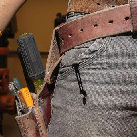Black folding pocket knife with belt clip, side view clipped to jeans pocket.
