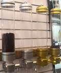 Wall Mounted Coffee Bean Dispenser With Clear Acrylic Shell And Tight Screw Lid To Keep The Stash Fresh, silver and gold, filled with beans.