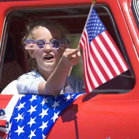 Child in car holding Cool 100 Pack Small American Flags On Sticks 8 By 12 Inch Mini US Flags With Solid Wooden Poles Safety Spear Tip