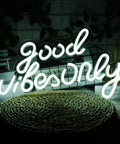 Good Vibes Only Neon Sign For Wall Decor Led Neon Light Brings Party Vibes To Your Living Room Bedroom Bar Game Room Restaurant Or Hotel White 16.5 By 10 Inches Easy Mount And Energy Efficient LED For Everyday Use And Party Ready Vibe on a table with trees in background