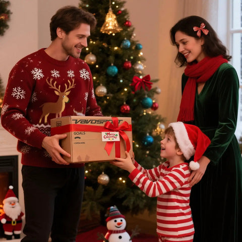 Family exchanging Christmas gift box in front of decorated tree, wearing festive sweaters and Santa hat, smile on child's face.