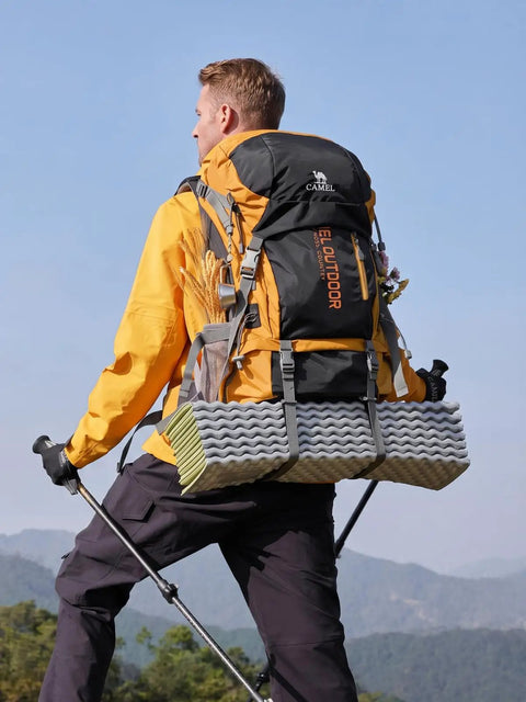 Person hiking with a 65L Internal Frame Hiking Backpack with rain cover, showing nylon material, in outdoor setting, wearing trekking poles.