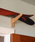Top Shelf Heavy Duty Bamboo Ski Wall Mount Rack For Garage Storage holding red and black skis on a beige wall.