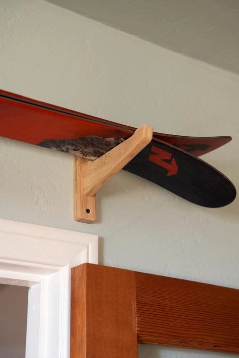 Top Shelf Heavy Duty Bamboo Ski Wall Mount Rack For Garage Storage holding red and black skis on a beige wall.