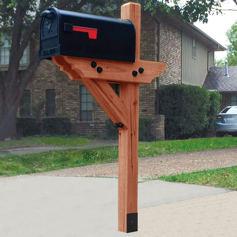 Wooden mailbox post with black mailbox, set on a concrete driveway with a brick house and greenery in the background.