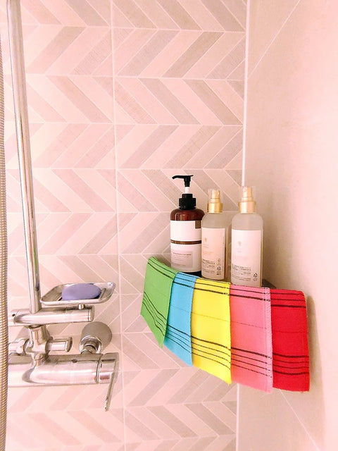 Five colorful bath towels on a rack in a tiled shower, with pump bottles nearby.