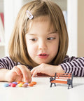Child observing Two Piece Miniature Park Bench Set For Fairy Gardens And Dollhouses on a table