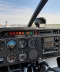Airplane cockpit controls with various gauges, switches, and dials, view of airport runway through windshield.