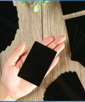 Hand holding a piece from the 300 Piece Aluminum Engraving Blanks Set For DIY Cards And Projects, 86 x 54 mm, 0.21 mm thick, black finish.
