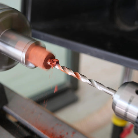 Close-up view of MT2 pen mandrel in wood lathe; 7mm drill bit cutting orange wood.