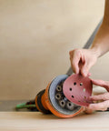 Person attaching 5 Inch Heavy Duty Random Orbit Sanding Discs With Hook And Loop Backing Red Resin Aluminum Oxide 8 Hole 40 Grit to sander