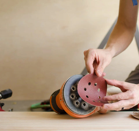 Person attaching 5 Inch Heavy Duty Random Orbit Sanding Discs With Hook And Loop Backing Red Resin Aluminum Oxide 8 Hole 40 Grit to sander