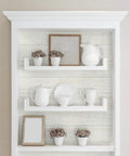 White Shiplap Peel and Stick Wallpaper Roll, DIY Friendly, displayed on shelves with white ceramics and decor in living room.