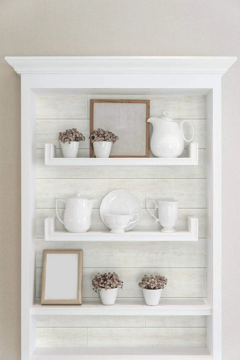 White Shiplap Peel and Stick Wallpaper Roll, DIY Friendly, displayed on shelves with white ceramics and decor in living room.