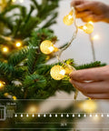 Hands decorating tree with Globe String Lights 60 LED Battery Operated With Remote 26ft Waterproof Indoor Outdoor Fairy