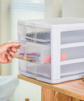 Hand opening a drawer of the 4 Pack 3 Drawer Stackable Plastic Organizer With Drawers White Frame Go To Countertop Storage Solution For Office Supplies Craft Rooms Classrooms And Home Organization placed on a desk.