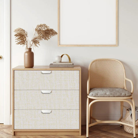 Cream Linen Textured Peel And Stick Wallpaper Roll 10Ft Long Beige Faux Grasscloth on cabinet next to a wicker chair.