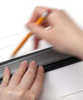 Person using a black ruler and pencil to draw lines on paper