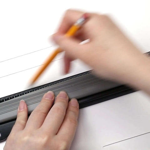 Person using a black ruler and pencil to draw lines on paper