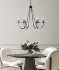 Black Six Light Farmhouse Chandelier With Candle Style Bulbs For Dining Room Bedroom And Living Room 28 Inch Wide And 24 And A Half Inch High Open Frame Iron Arms For A Dope Modern Rustic Look hanging above a dining table.