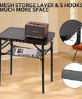 Foldable Picnic Table With Storage Net In Matte Black Aluminum Portable And Light For Camping Travel Or Indoor Use 23.6 By 15.8 Inches Three Height Settings Up To 27.5 Inches Fast Pack And Roll with items on top and mesh storage visible.