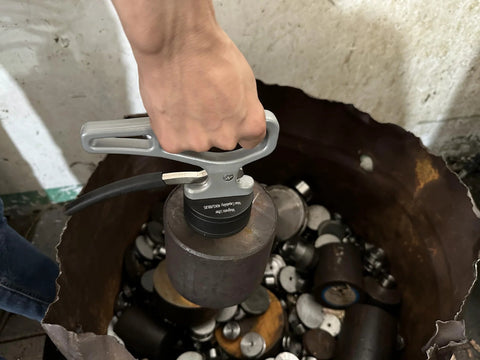 MUTUACTOR magnetic pickup tool with release handle, gray; front view lifting a metal piece from a bin.