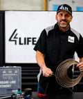 Person holding brake line coil in automotive workshop with 4LTL branded shirt, next to 1/4" brake line assortment case.