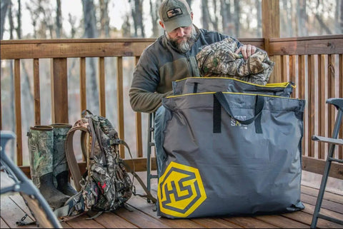 Man packing camouflage gear into Scent Safe Deluxe Travel Scent Bag For Hunting Gear And Clothing Keeps Your Scent Hidden And Your Gear Scent Free