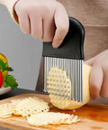 Crinkle cutter with black handle and stainless steel blades cutting a potato into crinkle fries