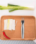 Mandoline slicer, stainless steel kitchen tool on a wooden tray with leek strips and a red pepper