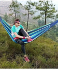 Person lounging in a durable portable cotton hammock for camping and outdoor indoor use with hanging ropes in a forest setting