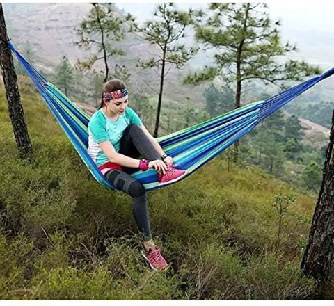 Person lounging in a durable portable cotton hammock for camping and outdoor indoor use with hanging ropes in a forest setting
