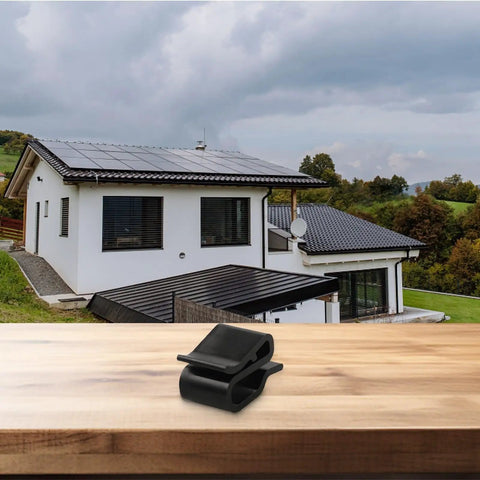 Rock Solid Solar Cable Clamps And Wire Clips For PV Panels on wooden table with a house featuring solar panels in background.