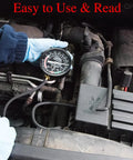 Close-up of VECKYJL vacuum gauge tester in a car engine bay, held by a blue-gloved hand with hoses connected.